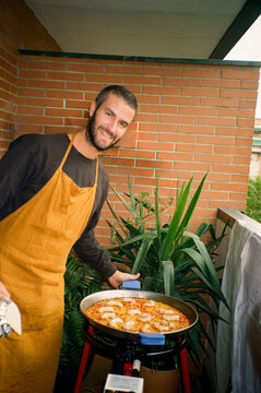 Analog flash portrait of a man posing next to a casserole with paella
