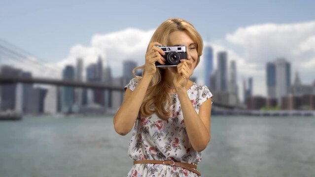 Portrait of a blonde woman with a retro photo camera. Big city river in the background.
