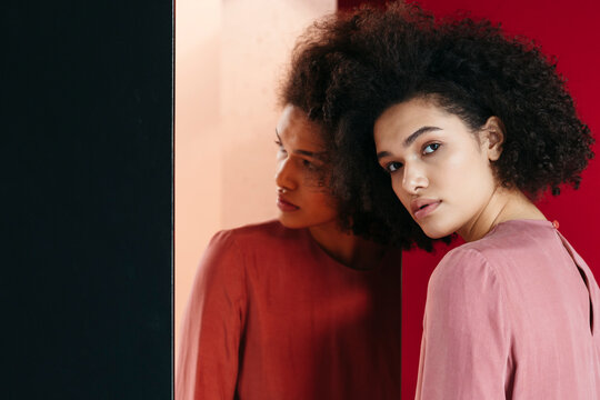 Contemplative Woman With Curly Hair Beside Red Backdrop