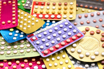 Oral contraceptive pill on pharmacy counter with colorful pills strips background.