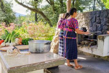 Two Latin women in front of a handmade stove prepare to cook.