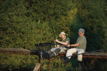 Two fishermen with fishing rods on a footbridge near the lake at summer