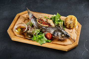 Rainbow trout stuffed with vegetables and pomegranate seeds, accompanied by a salad, served on a wooden tray with a black background. A healthy, colorful dish that's a feast for the eyes