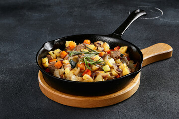Savory cast-iron skillet ragout with tender meat and colorful vegetables on a textured black table