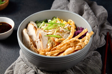 Asian salad bowl with chicken fillet, soybean sprouts, corn, cabbage, and green onions on a gray cloth
