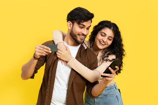 Excited Couple Sharing Credit Card Details On Phone For Online Shopping On Yellow Background. E-Commerce, Shopping, Young Adults