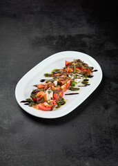 Traditional italian food - caprese salad with mozzarella cheese, tomatoes and pesto sauce. Caprese salad on black concrete background in minimal style. Italian appetizer caprese on dark background