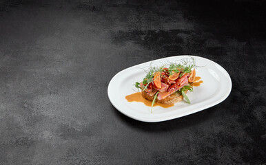 Tuna bruschetta on white plate with sauce on black background. Appetizers with crispy bread and sliced tuna fish. Traditional antipasti - fish bruschetta on dark concrete table. Tuna bruschetta.