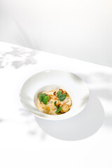 Seafood risotto with scallops and cauliflowers on white plate. Creamy risotto with sea scallops and cauliflowers. Italian risotto with sea scallops on light background with shadows of leaves