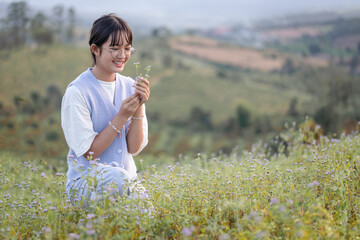 Smiling pretty girl teenager with glasses sitting in field holding grass flower outdoor