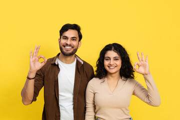 Happy Couple Showing Okay Sign Against Yellow Background - Positive Gesture, Relationship, and...
