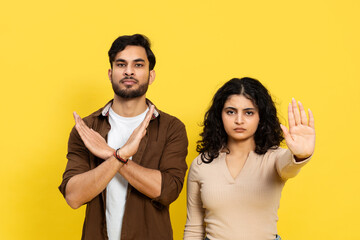 Young man and woman making stop gestures against a yellow background, expressing denial and...