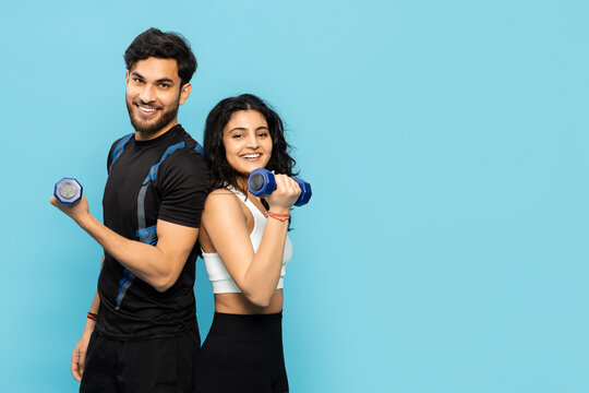 A Happy, Energetic Couple Engages In A Fun Workout Session, Holding Dumbbells And Smiling Against A Vibrant Blue Background. This Image Captures The Concept Of Fitness, Exercise, And Shared Wellness.