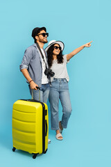 Couple On Vacation Pointing Away With Yellow Suitcase On Blue Background
