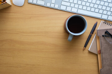 Simple workplace with keyboard, glasses, notebook and cup of coffee on wooden desk. Top view with...