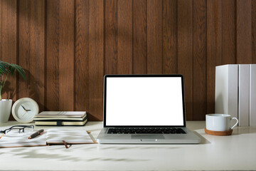 Laptop with white blank screen, notebook, coffee cup and glasses on wooden table.