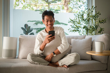 Happy millennial asian man typing message or ordering food delivery on smart phone while sitting in...