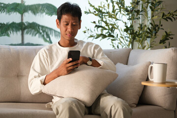 Happy relaxed man sitting on couch at cozy home and using mobile phone.