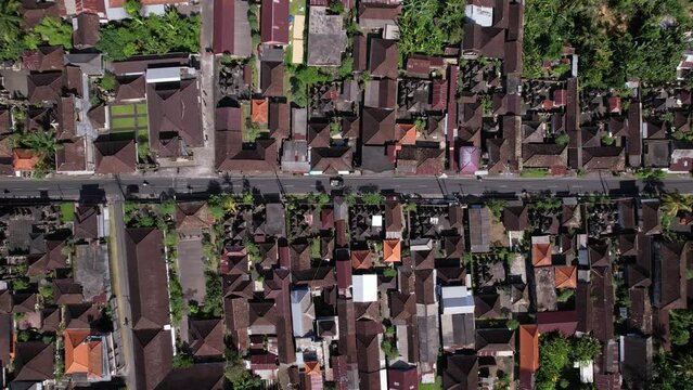 Aerial shot of Balinese town, panning plan view from drone, map-like picture of numerous house compounds build along straight road. Low rise buildings, roofs covered with tiles