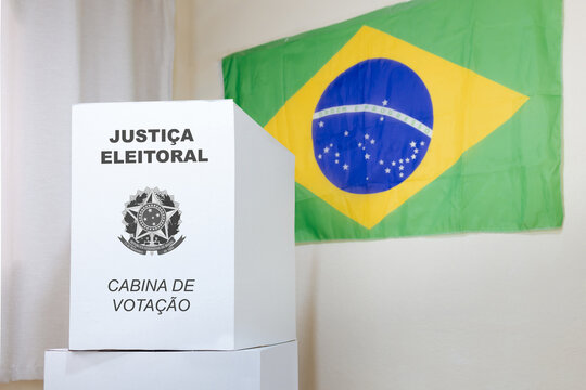 Cabine de vota&ccedil;&atilde;o da urna eletr&ocirc;nica brasileira, com uma parede decorada com a bandeira do Brasil. A imagem retrata a democracia e o processo eleitoral no Brasil, simbolizado pela cabine de vota&ccedil;&atilde;o.