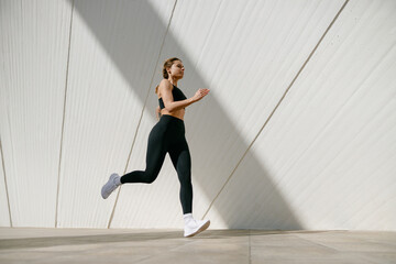 Active woman athlete is jogging on morning on modern building background. Healthy life concept