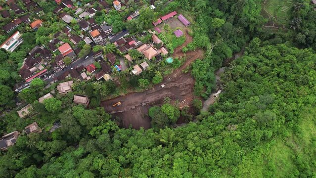 One excavator works on slope of ravine, removing soft soil and digging down to rock. Aerial view of earthworks, beginning construction of buildings at West Wos River gorge and Campuhan ridge area