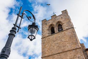 Medieval church tower and electric street lamp as a stork flies through the sky. Aranda. - obrazy, fototapety, plakaty