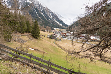 View from the Besinnungsweg trail in Längenfeld-Gries im Sellrain toward Gries village. Early springtime view, with snowcapped mountains in the background. Grassy slopes and pine trees.