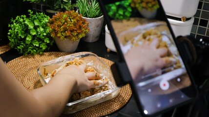 Close up of a female food vlogger filming herself cooking in the kitchen with her smartphone for...