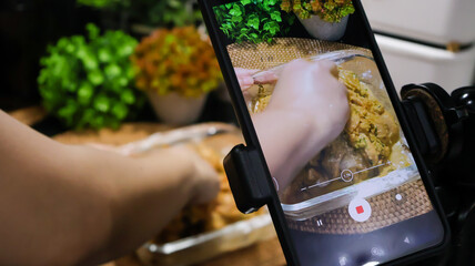 Close up of a female food vlogger filming herself cooking in the kitchen with her smartphone for the social media platform. A female homecook creating content video in her kitchen at home.