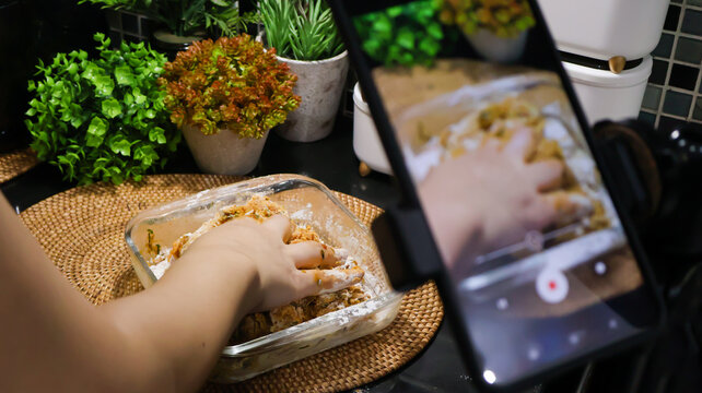 Close up of a female food vlogger filming herself cooking in the kitchen with her smartphone for the social media platform. A female homecook creating content video in her kitchen at home.