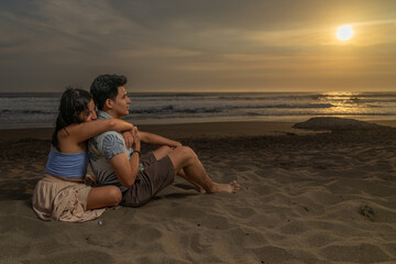 Fototapeta premium Couple in love sitting on the sand embracing looking at the sea