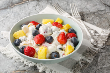 Cream cheese salad with strawberries, blueberries, pineapple close-up in a bowl on a marble table. Horizontal