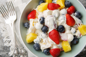 Summer cheesecake salad with strawberries, blueberries, pineapple, dressed with cream cheese and cream close-up in a bowl on a marble table. Horizontal top view from above