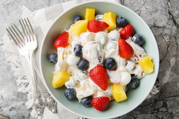 Hawaiian Berry Cheesecake Salad with strawberries, blueberries, pineapple, dressed with whipped cream cheese close-up in a bowl on a marble table. Horizontal top view from above
