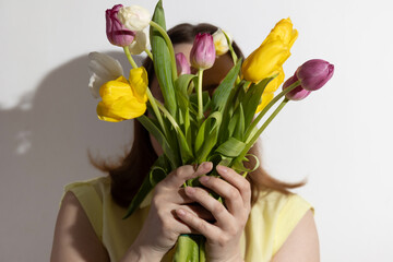 A woman smells colorful tulips in her hands in a room illuminated by sunlight. High quality photo