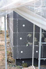 A wall of a house covered with EPS graphite polystyrene boards for thermal insulation, a scaffolding and building safety scaffolding net, anchors, an exterior wall mounted water faucet