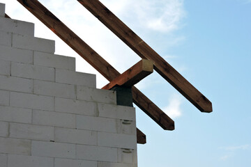 Wooden rafters and a wall plate, walls made of autoclaved aerated concrete blocks, blue sky in the background
