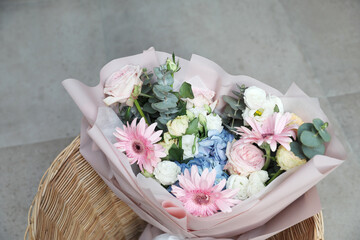Mixed colorful flower bouquet in basket on gray tiled floor background