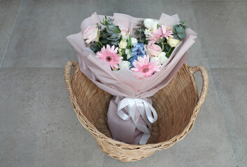 Mixed colorful flower bouquet in basket on gray tiled floor background