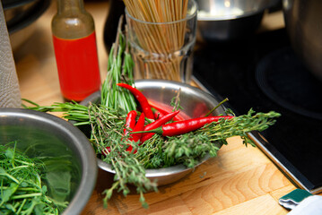 Kitchen Prep with Fresh Herbs and Chili Peppers. A chef's kitchen setup featuring a bowl of fresh herbs and red chili peppers, with cooking utensils in the background.