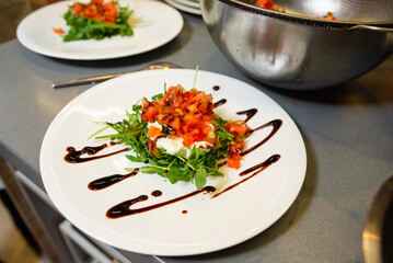 Arugula Salad with Tomato and Cheese Garnish. A refreshing arugula salad topped with diced tomatoes and cheese, drizzled with a balsamic glaze, served on a white plate.
