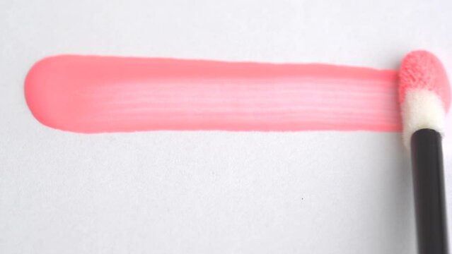 Cosmetic liquid lip gloss, lipstick smudge of peach fuzz color, smear, stroke. Smears of pink lip gloss applicator on a white background