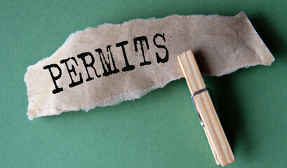 PERMITS - word on a torn brown piece of paper with a clothespin on a green background
