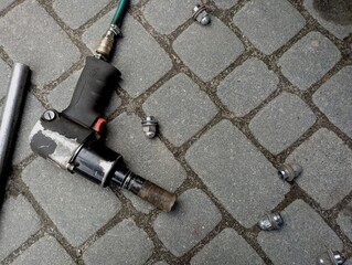 A pneumatic device for unscrewing bolts and screws lies on the cobblestones in the yard next to the...
