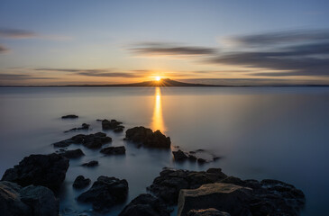 Long exposure image of sunrise over the top of Rangitoto Island. Takapuna Beach. Auckland.