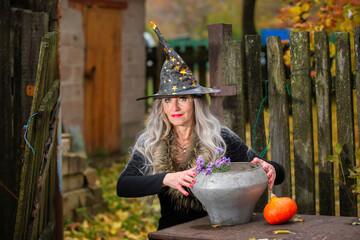 Halloween girl with a magic bowler hat in a witch hat performs witchcraft against an old creepy...