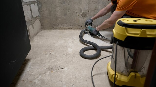 A worker smoothest the floor with an angle grinder. Grinding a concrete floor with a grinding machine before repair. A worker polishes the surface of a concrete floor before laying parquet.