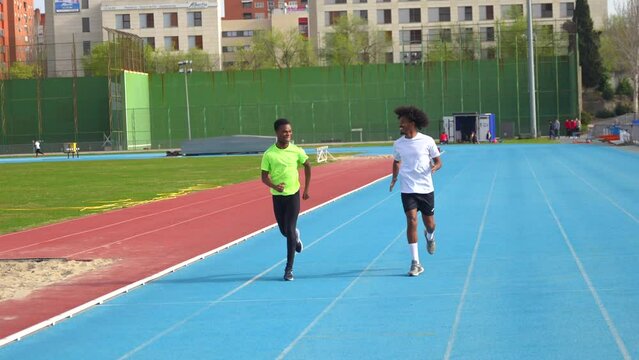 Full length video of two smiling young african runners training together in an outdoors athletics track