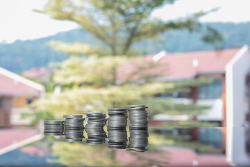 Stacked coins on the glass table creating a reflection. Housing development in the background.